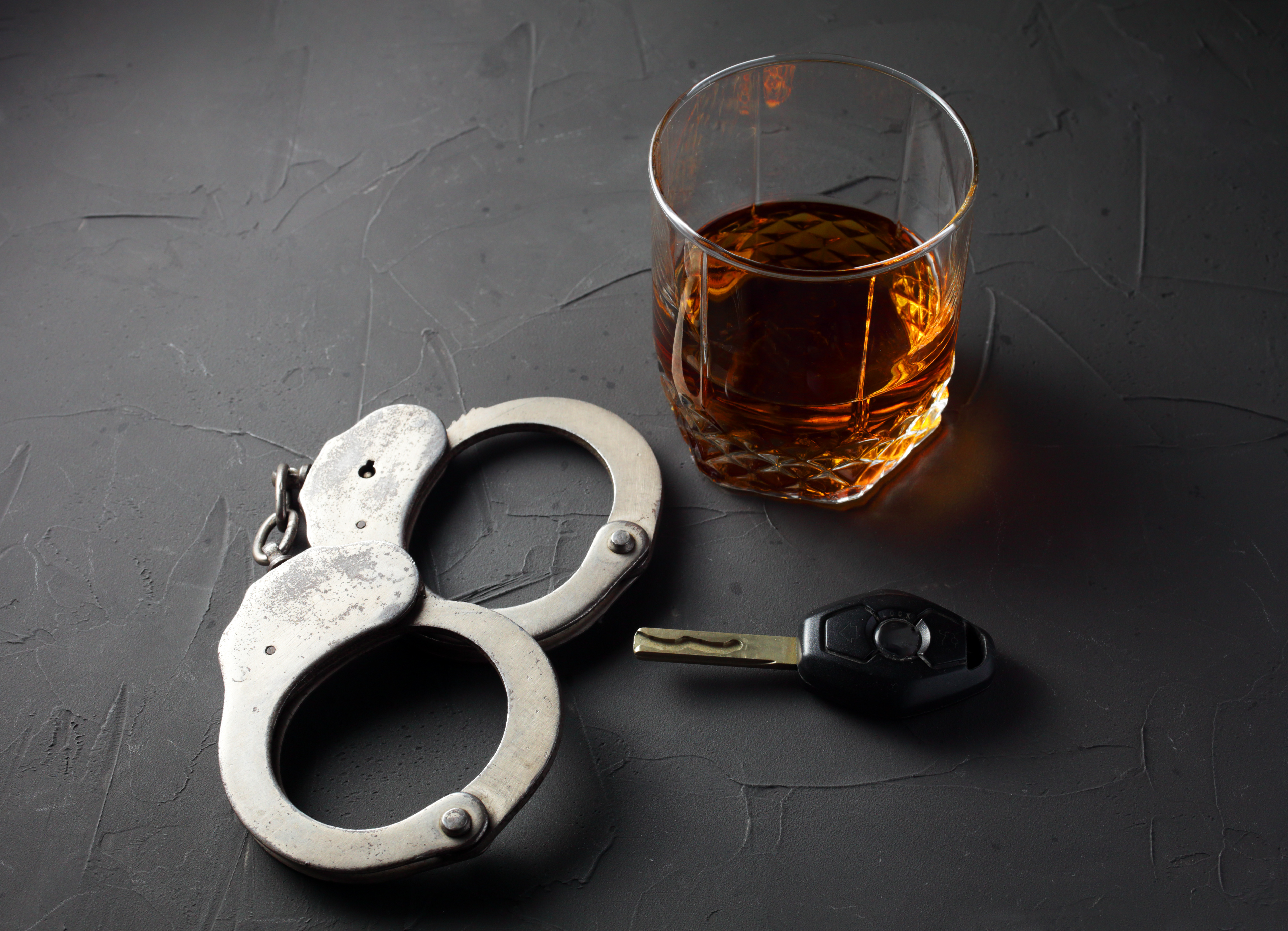 A glass of alcohol sitting on a table next to a pair of keys and handcuffs.